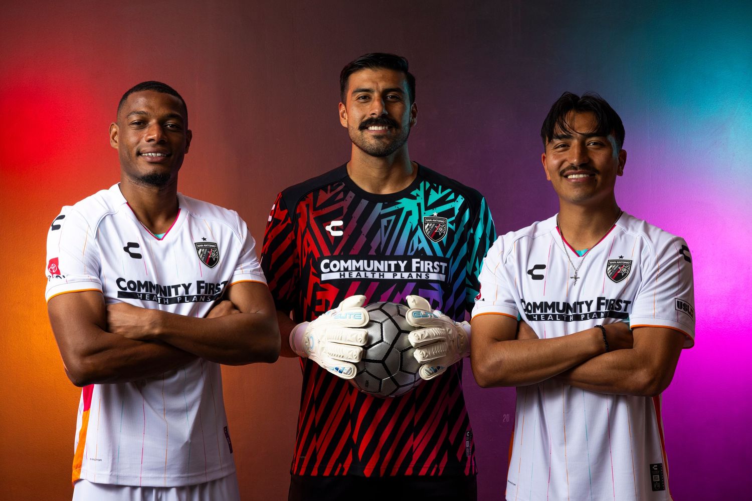 Three soccer players pose in team uniforms against colorful gradient background.