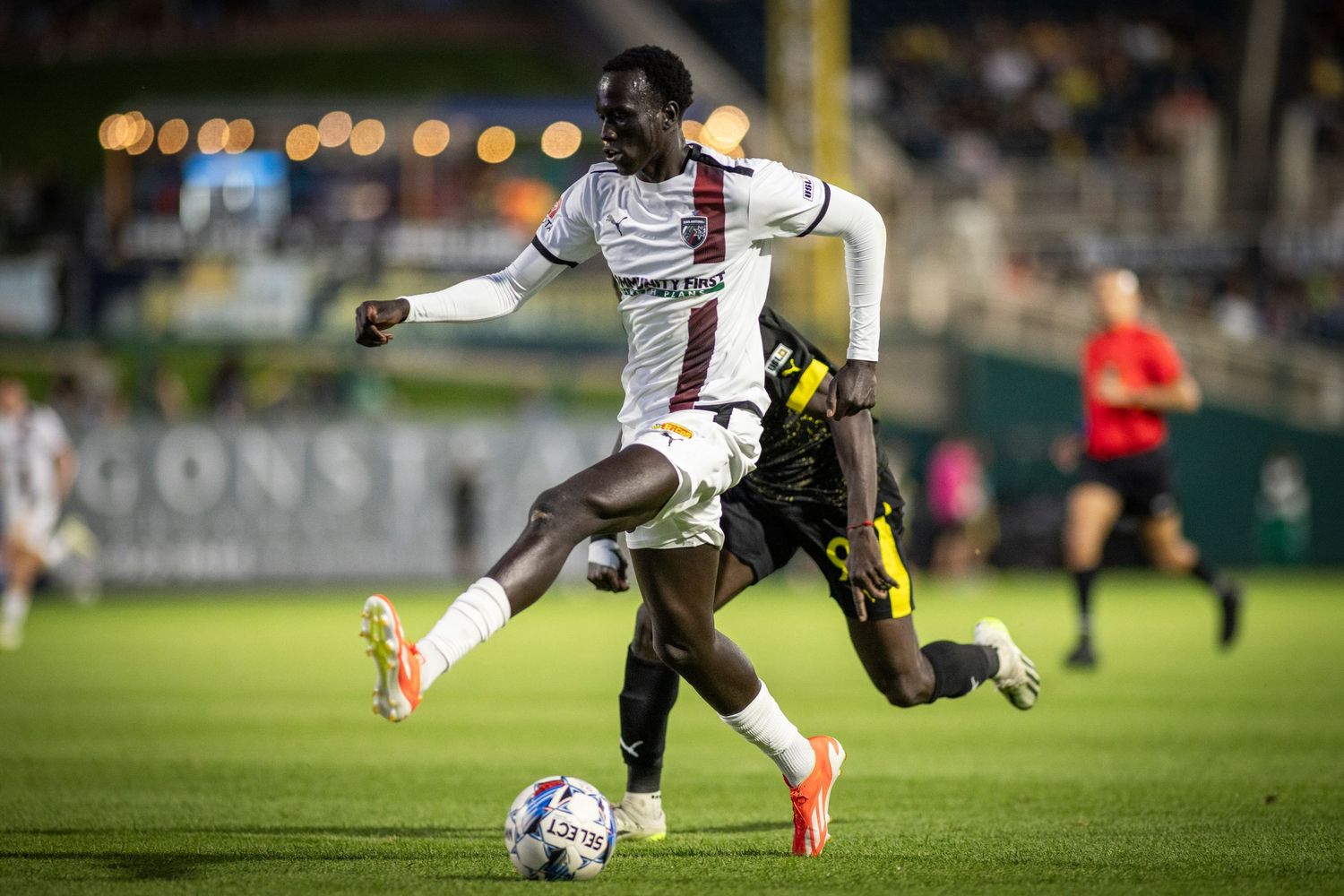 Soccer players battle for ball possession during an evening match under stadium lights.
