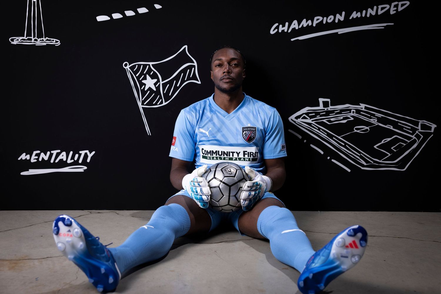 Soccer player in light blue uniform sits against wall with chalk drawings.