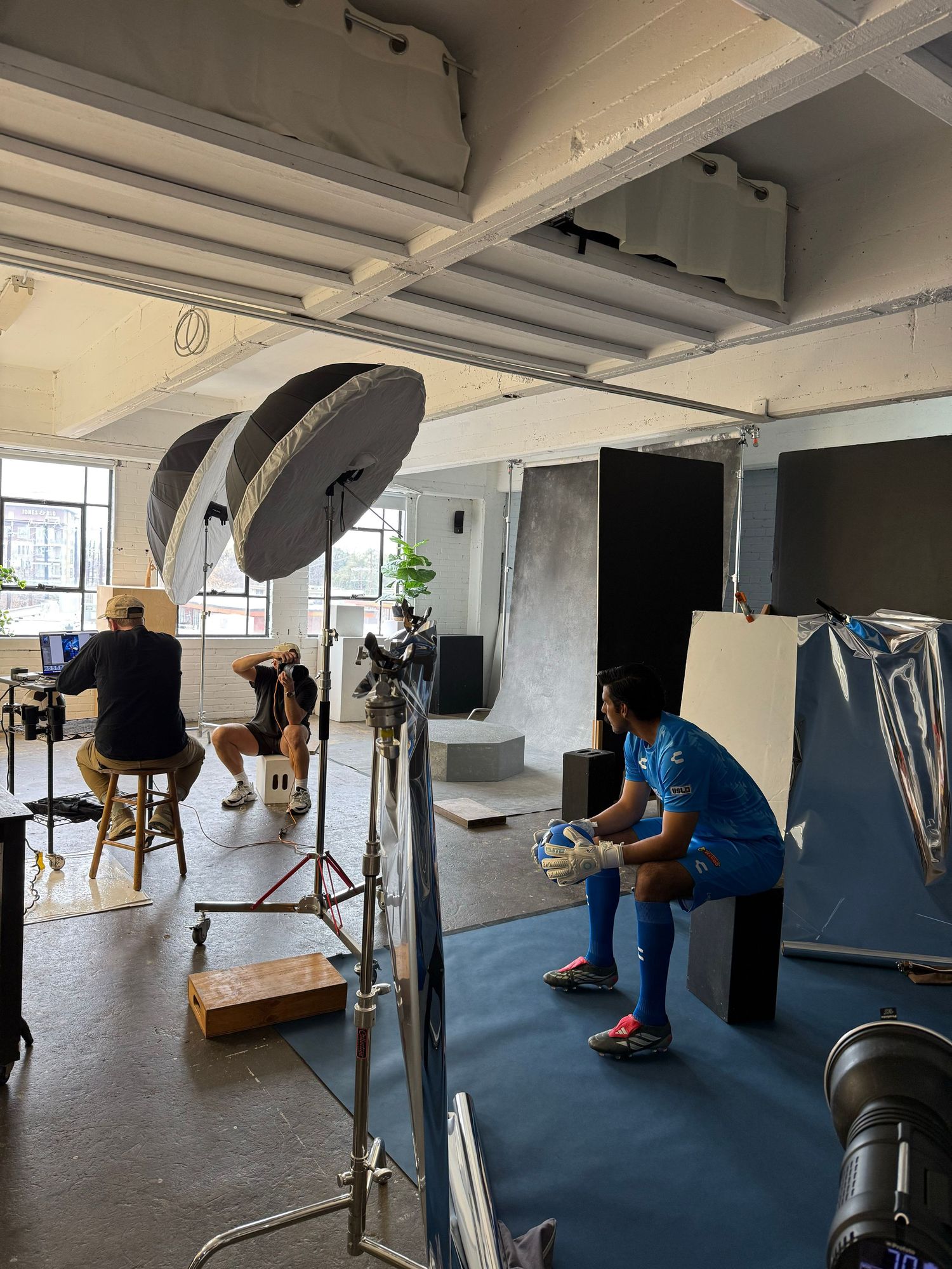 Professional photo studio shoot with athletes in sports gear, studio lighting equipment, and photographers working in background.