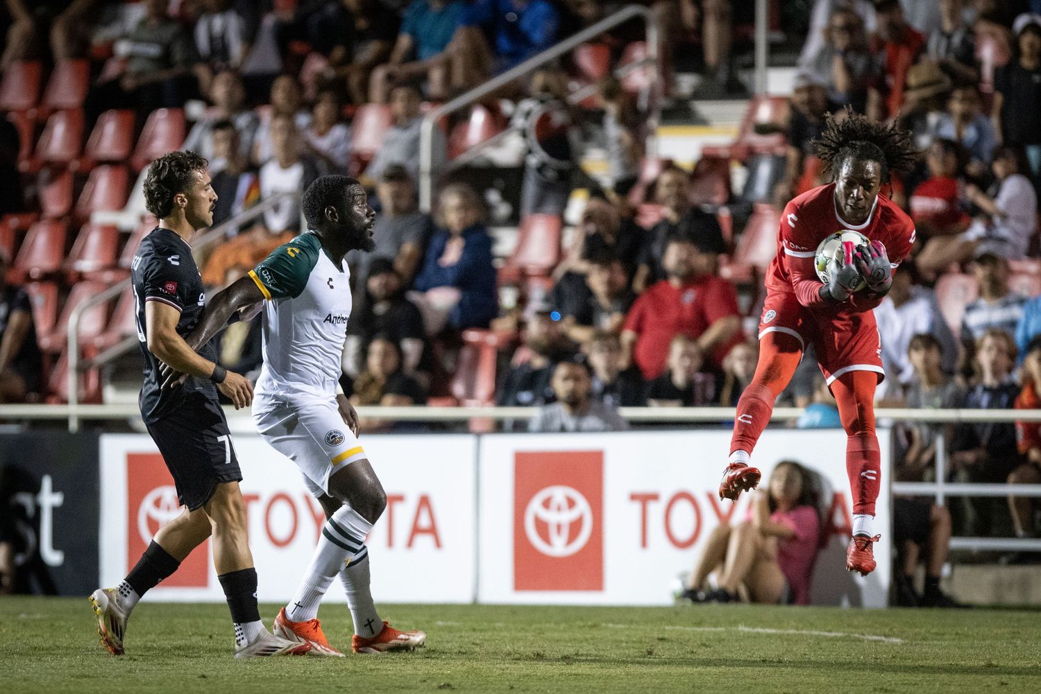 Soccer players compete for the ball during a match with Toyota advertising boards visible.