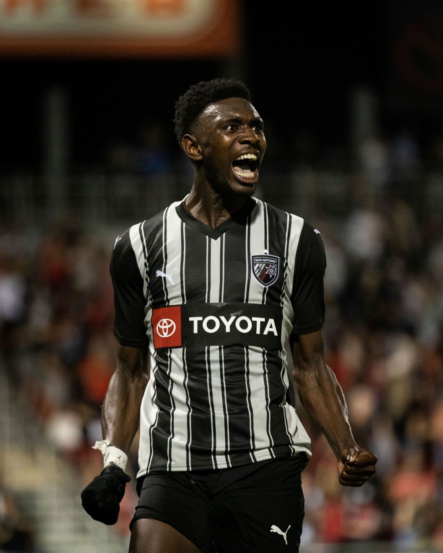 Player in black and white striped Toyota jersey celebrates passionately during match.