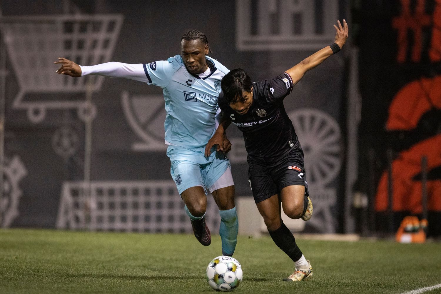 Two soccer players battling for ball control during a night game.