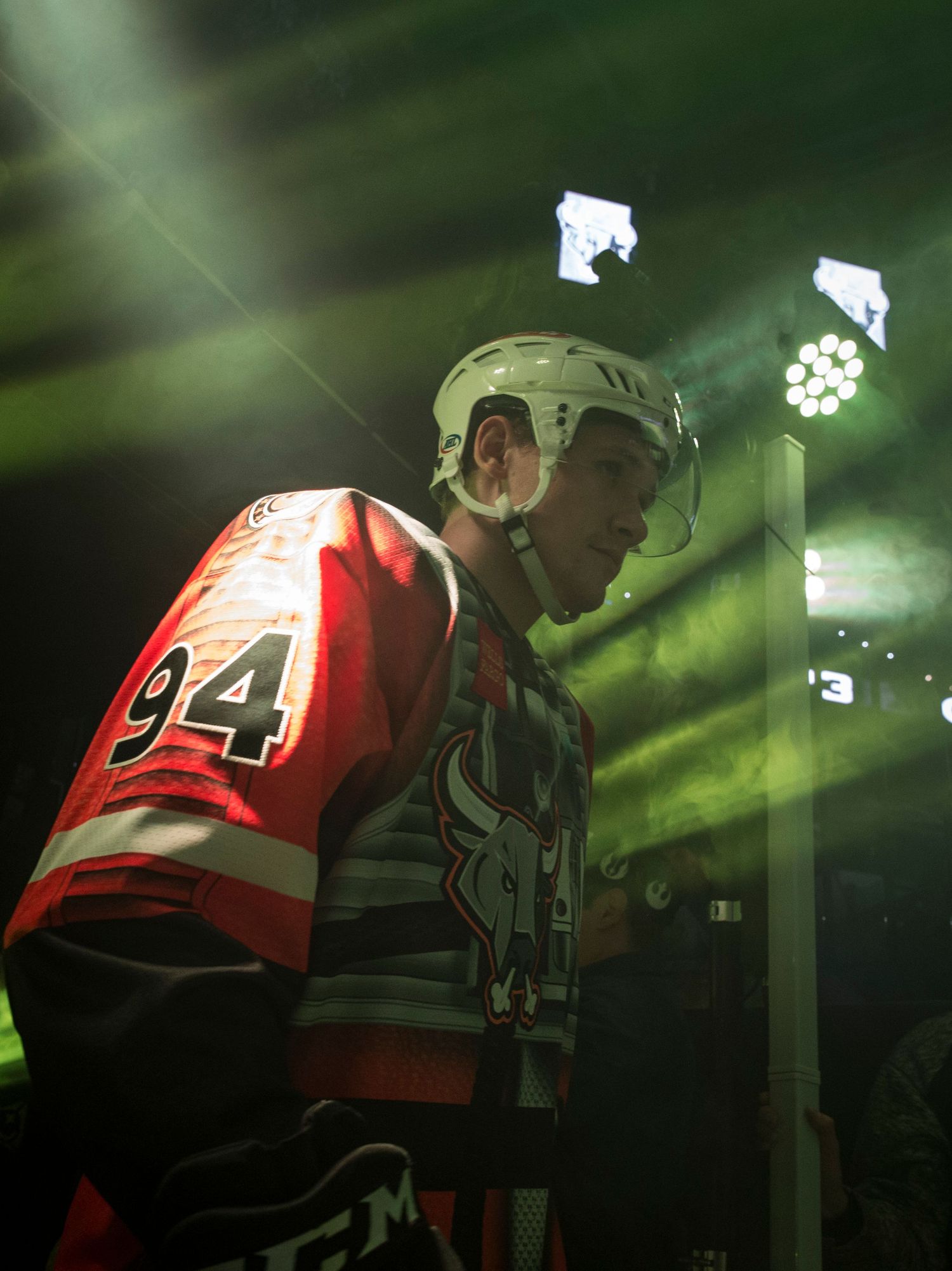 Hockey player in red jersey illuminated by green arena lights.