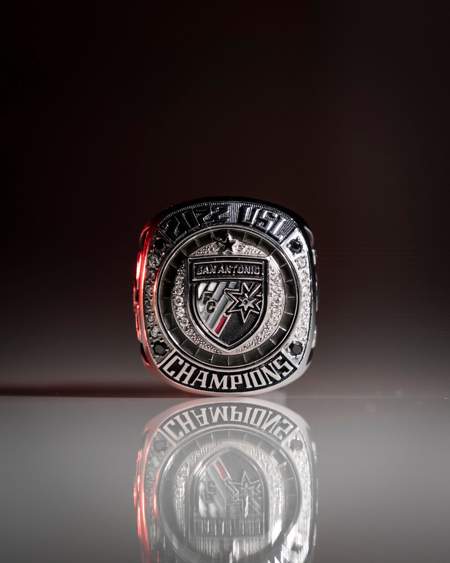Championship ring with detailed metalwork reflecting on dark surface.