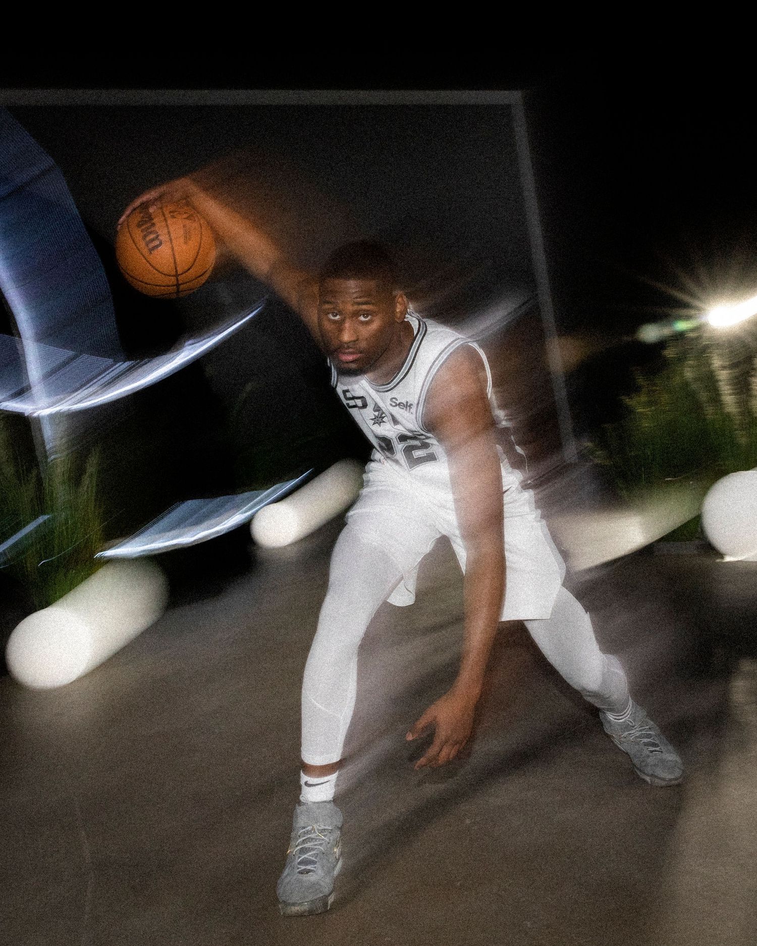Motion-blur action shot of Spurs player dribbling basketball in white uniform.