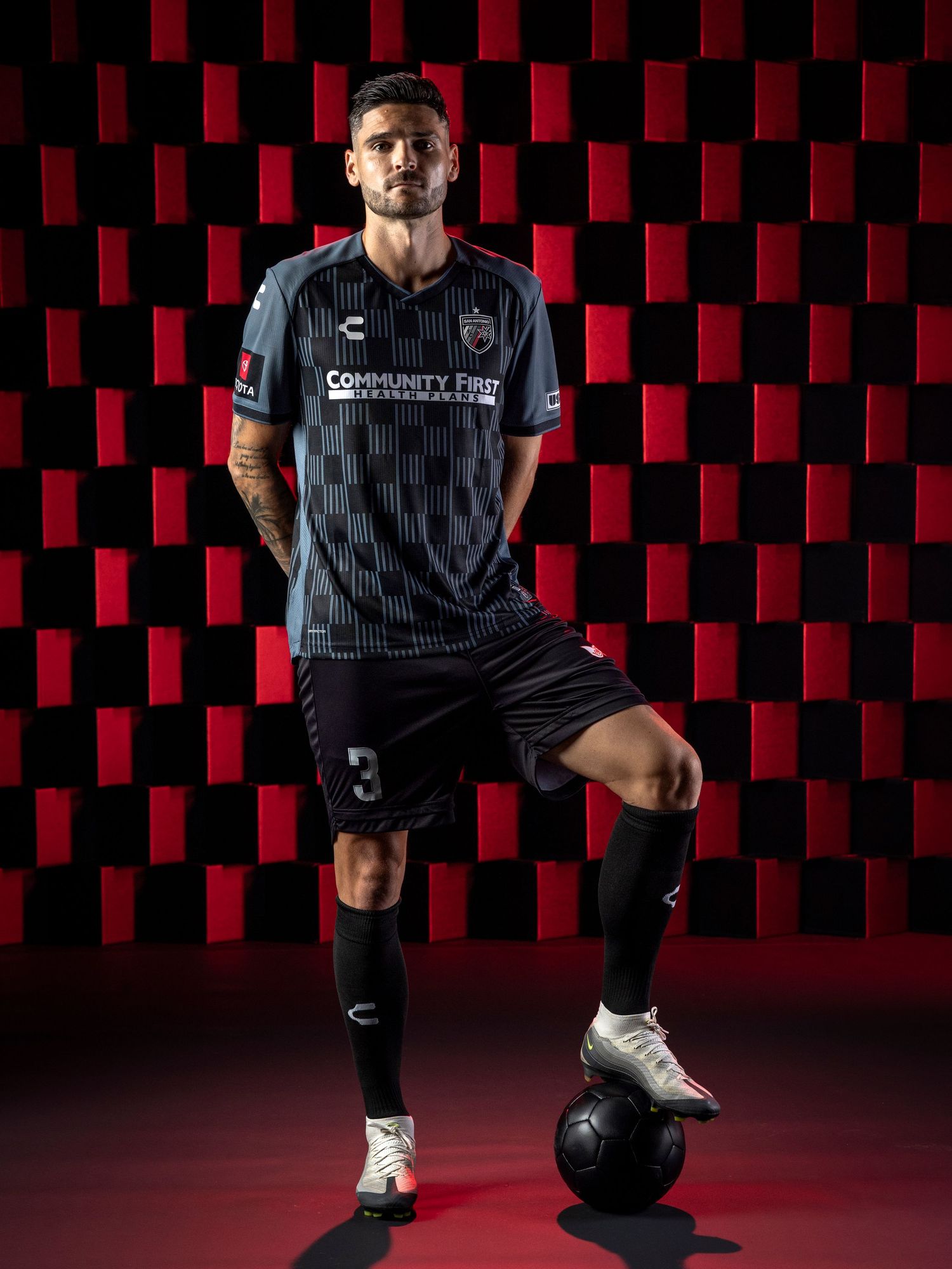 Professional soccer jersey design showcasing black striped pattern, against a red checkered background. SAFC, USL, MLS, CHARLY Futbol