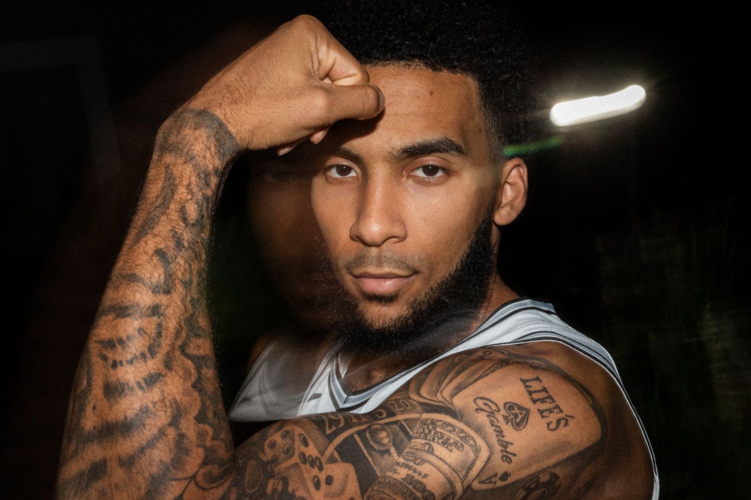 Basketball player with tattooed arm poses in dramatic lighting during team photoshoot.