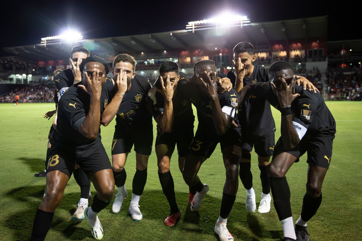 Soccer players pose for a celebratory team photo under stadium lights at night.