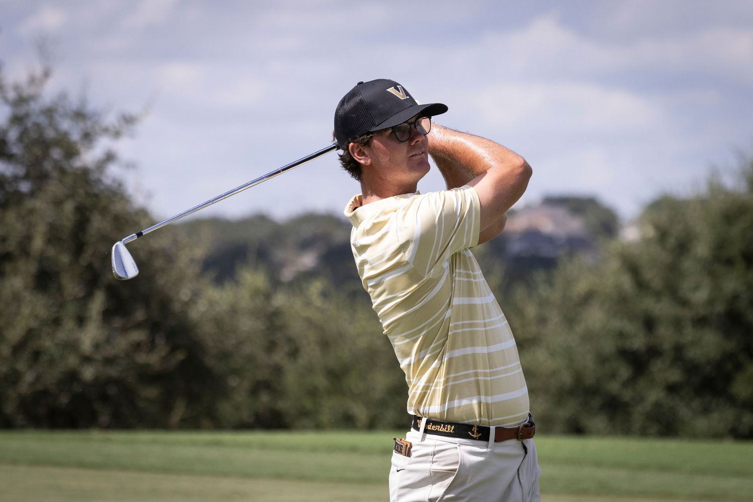 Golfer in light colored outfit executes perfect swing form on golf course.