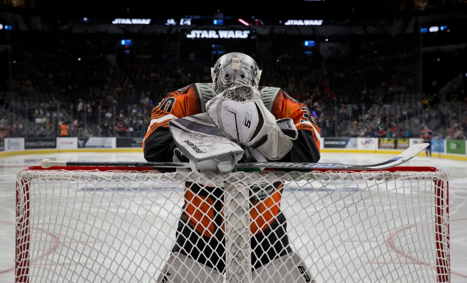 A hockey goalie rests on top of the goal net during a game.