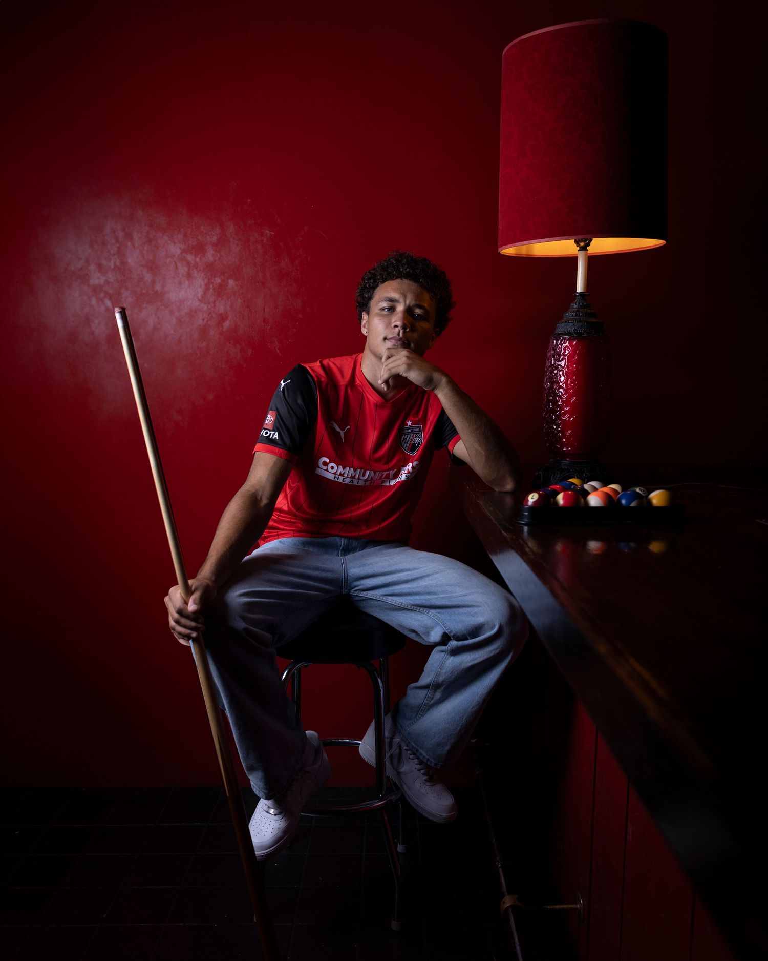 Athlete poses with pool cue in red-themed billiards room setting.