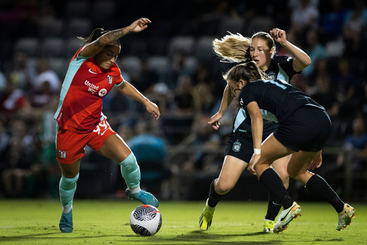 Women's soccer match action showing player in red attempting to dribble past defender in dark uniform.