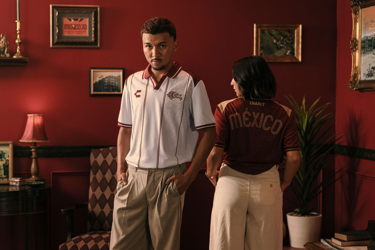 Two people in Mexico jerseys stand in a red-walled room with vintage decor.