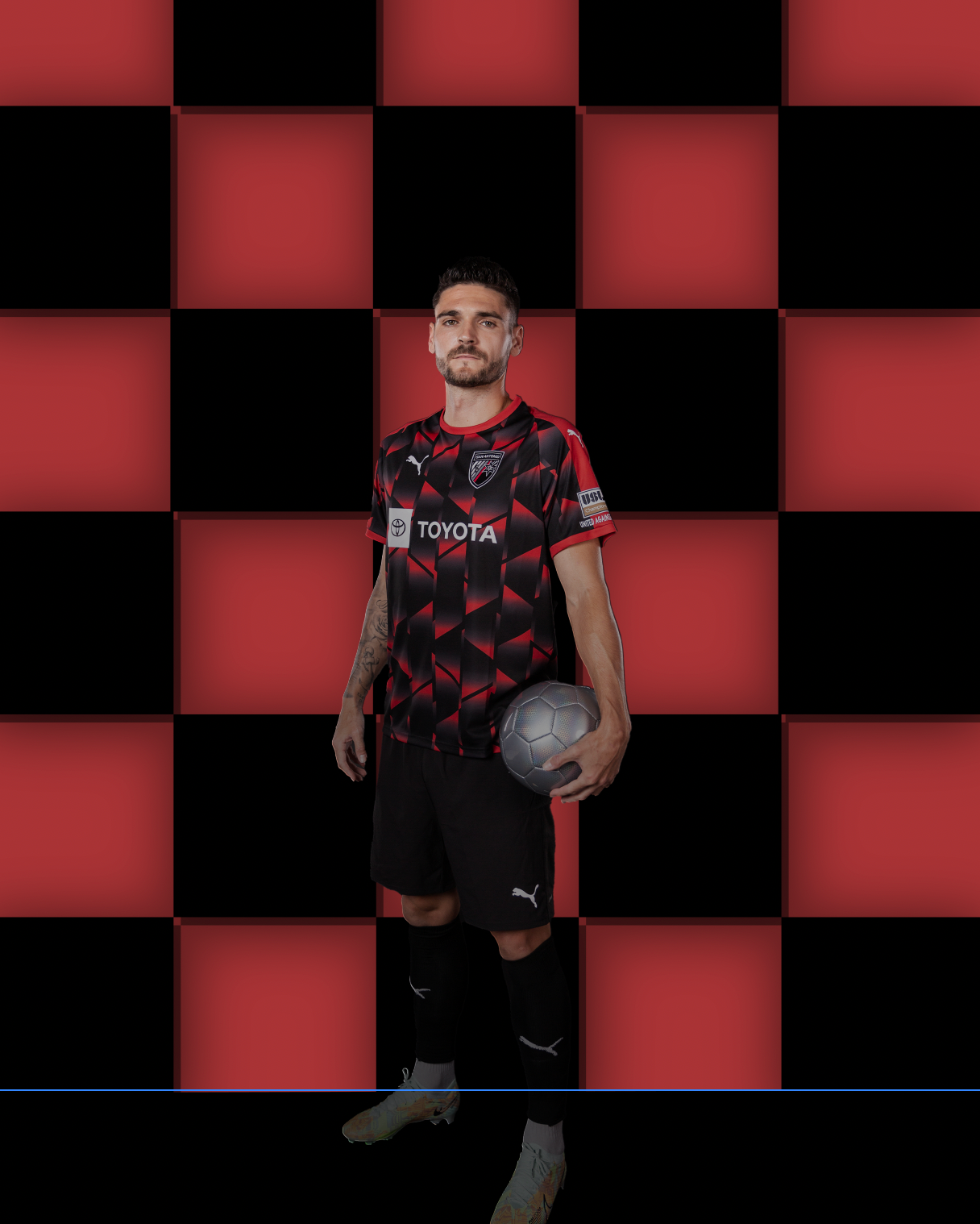 Soccer player poses in red and black geometric patterned jersey against checkered background.