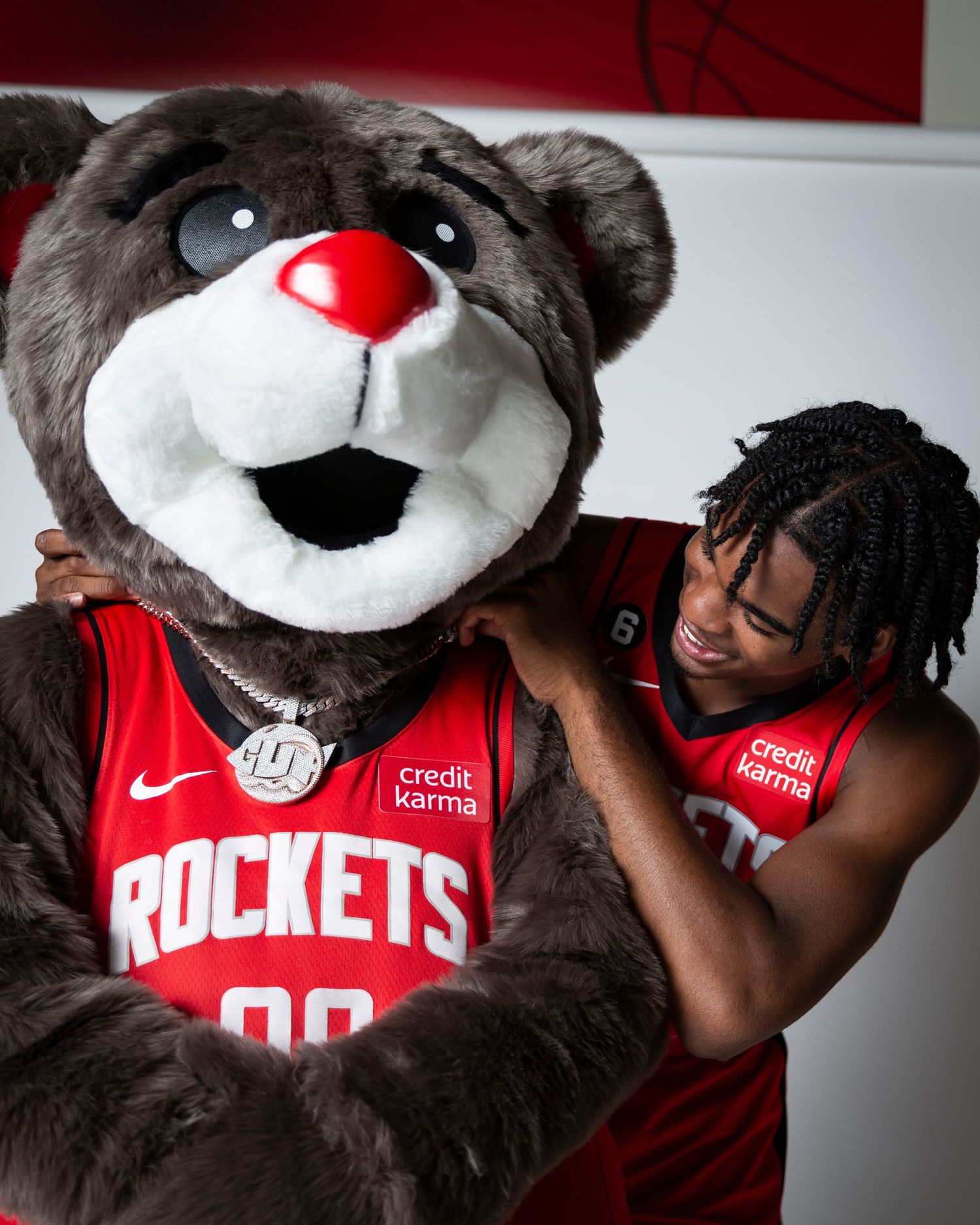 Basketball player poses playfully with Rockets mascot during team photo session.