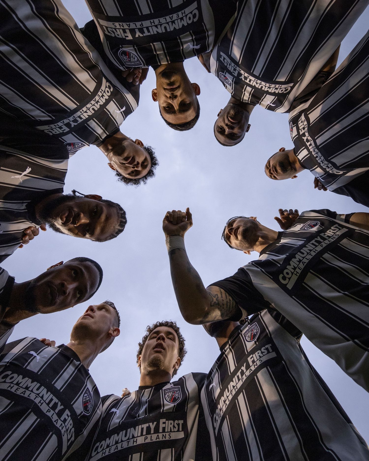 Soccer team huddles in a circle formation shot from below against bright sky.