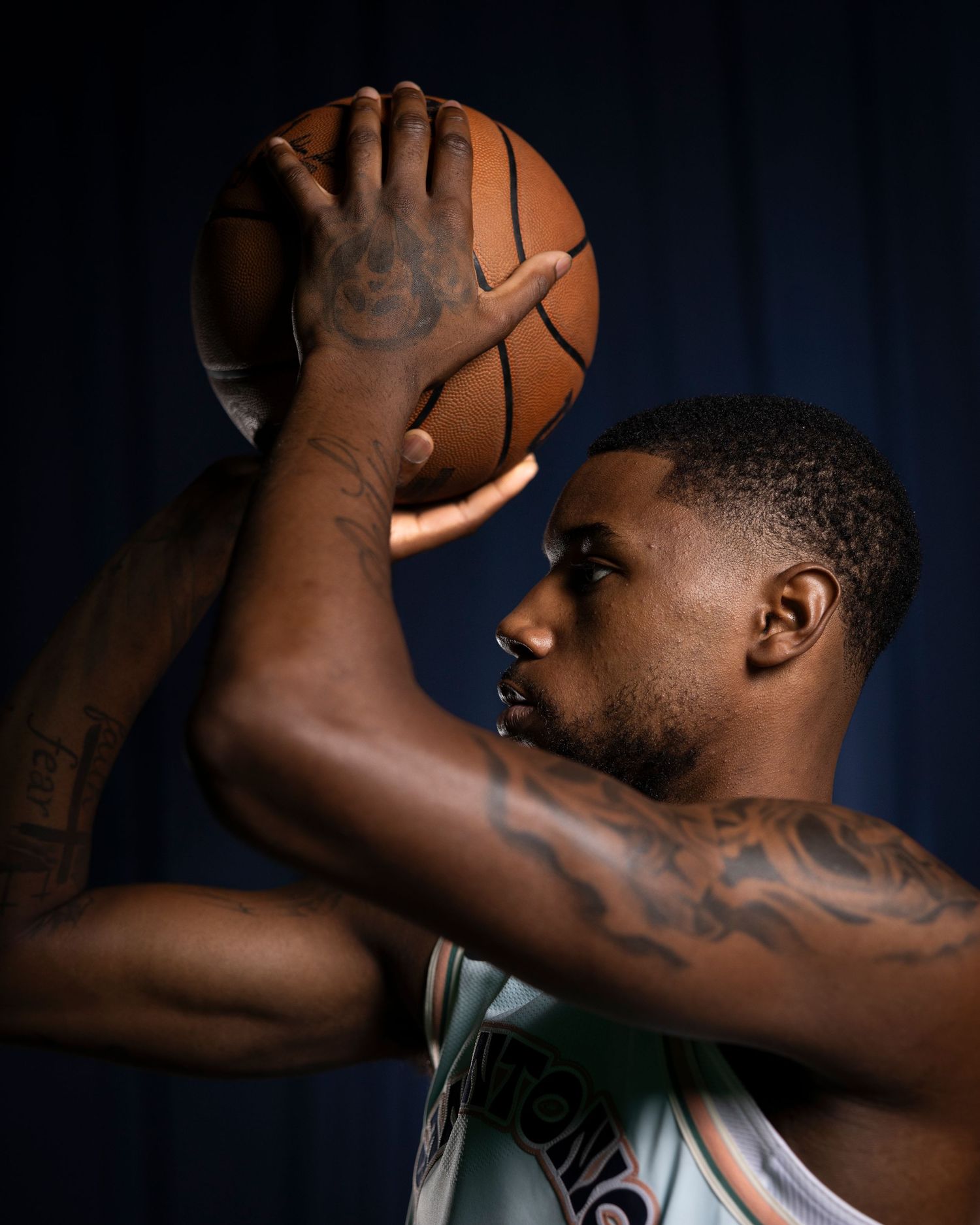Basketball player with tattoos holding ball in dramatic lighting against dark background.