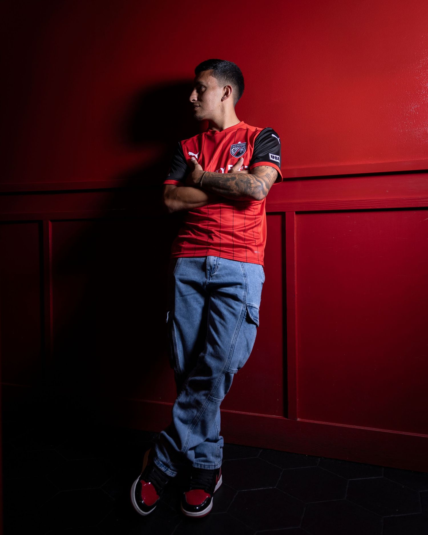 Professional athlete in red jersey leans against red wall in dramatic lighting.