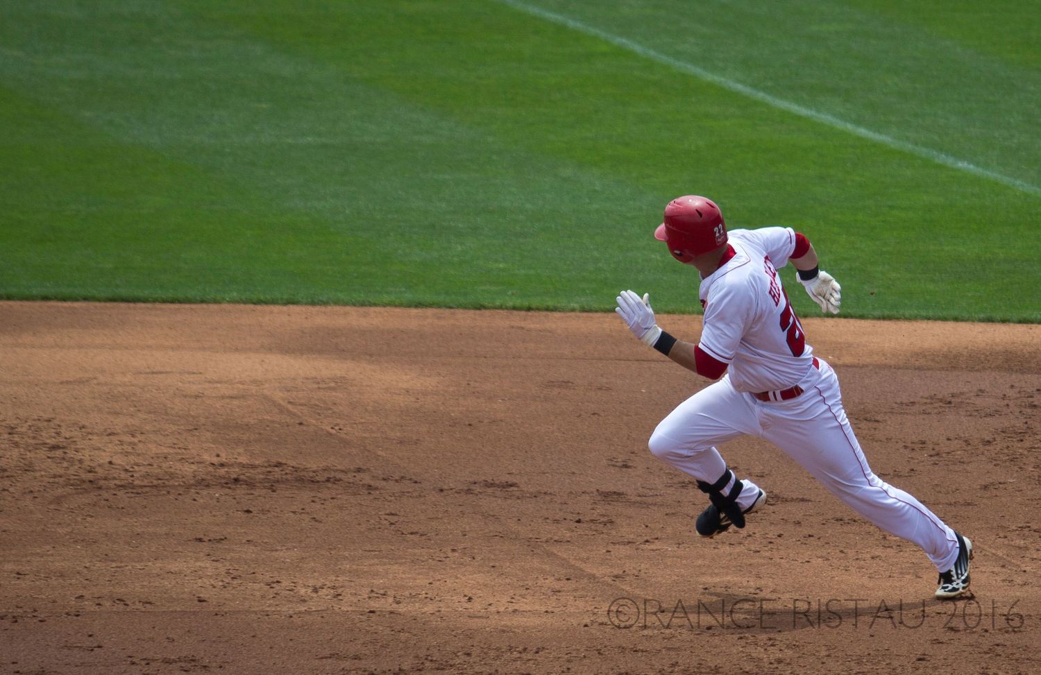 Baseball player in white uniform running on base path during game.
