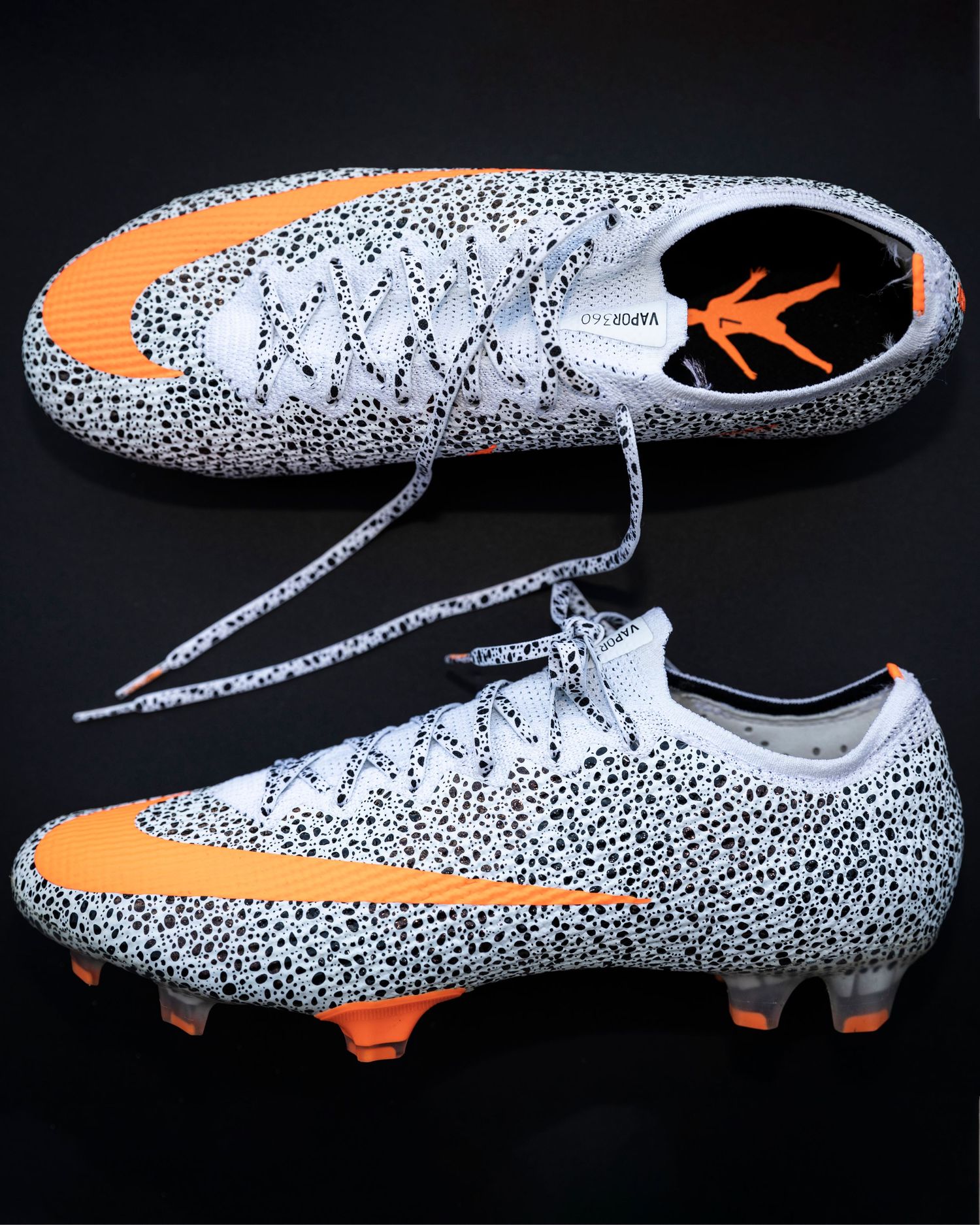 Safari-themed soccer cleats with orange accents displayed against black background.