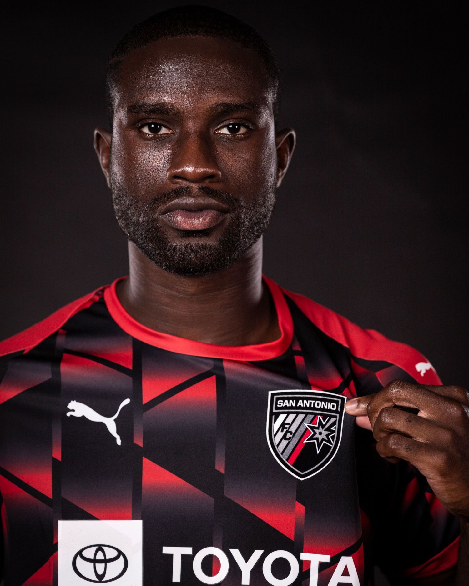 Professional soccer player poses in red and black San Antonio FC jersey with Toyota logo.
