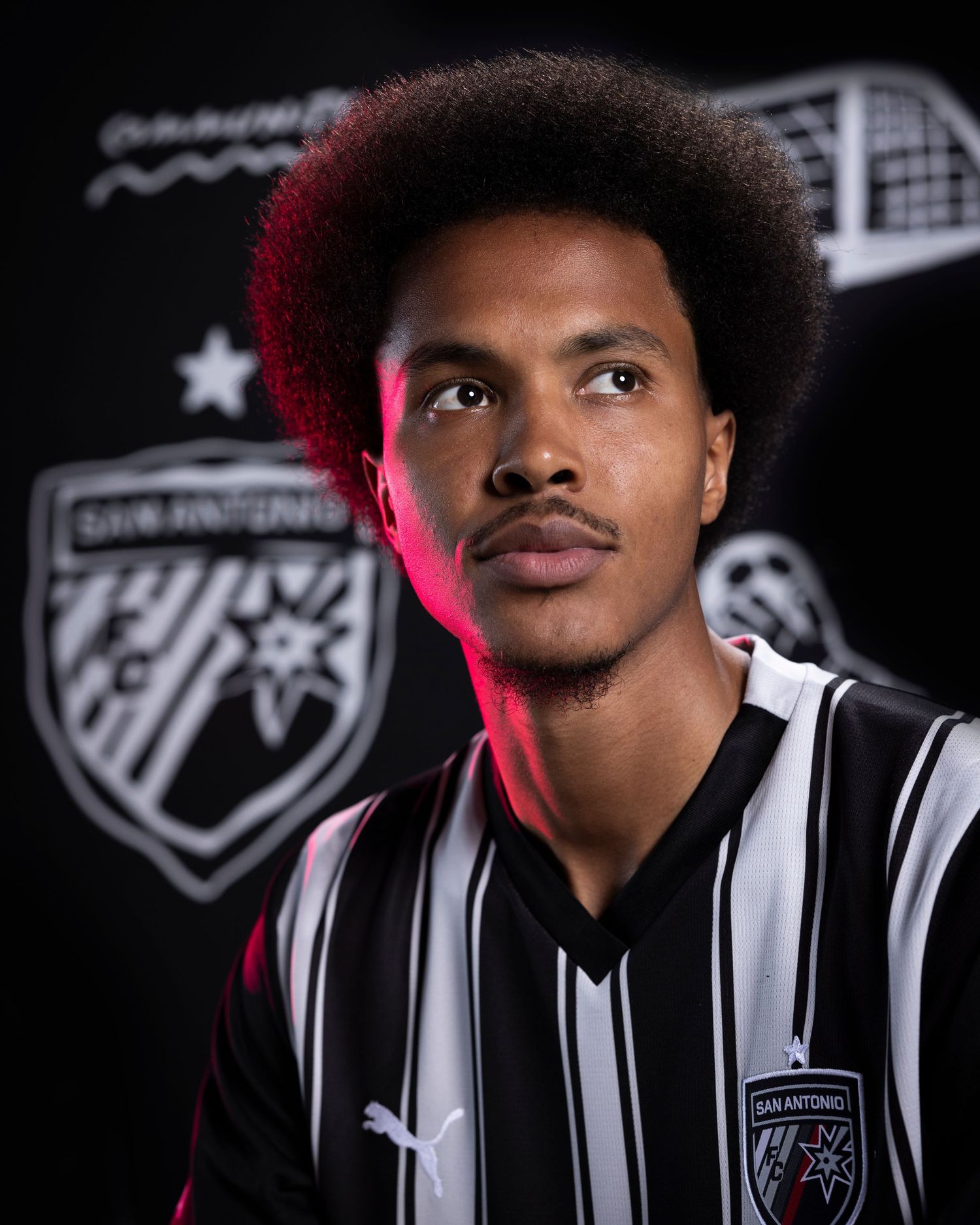 Soccer player in striped jersey against dark background with team logo and pink lighting.