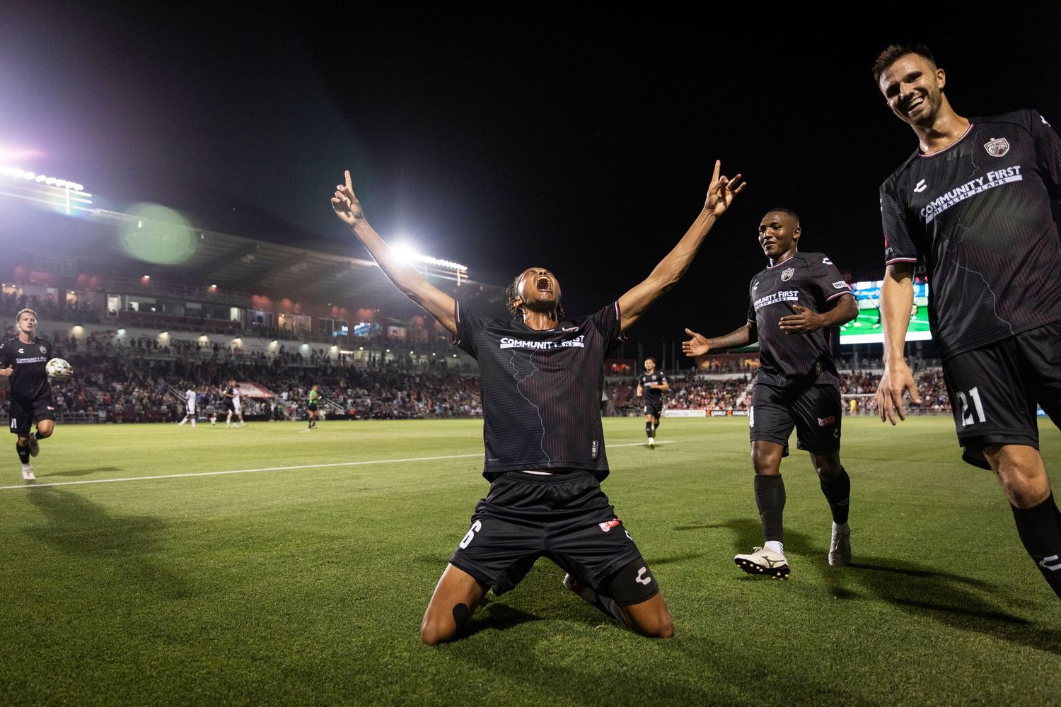 Soccer players celebrate goal with passionate celebration in night game.