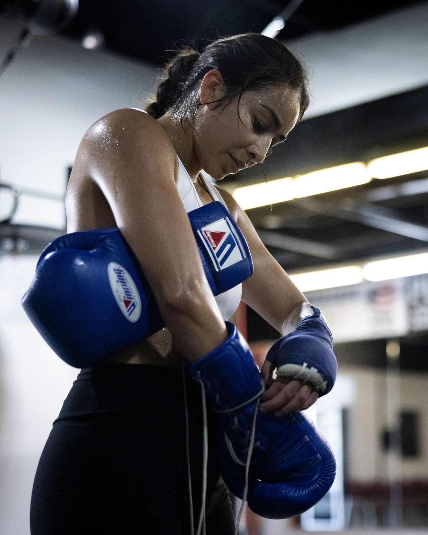 Athlete adjusting blue boxing gloves during training session in gym.