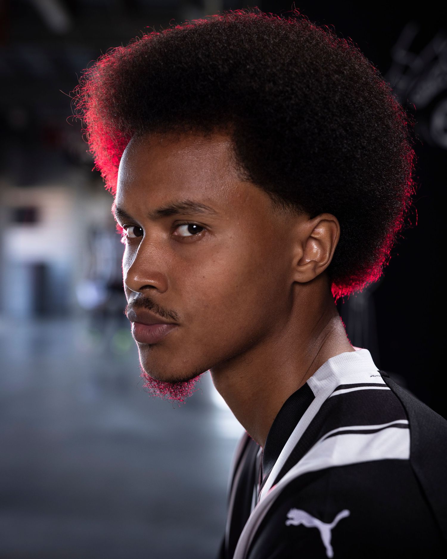 Side profile portrait of athlete with afro hairstyle wearing striped Puma jersey.