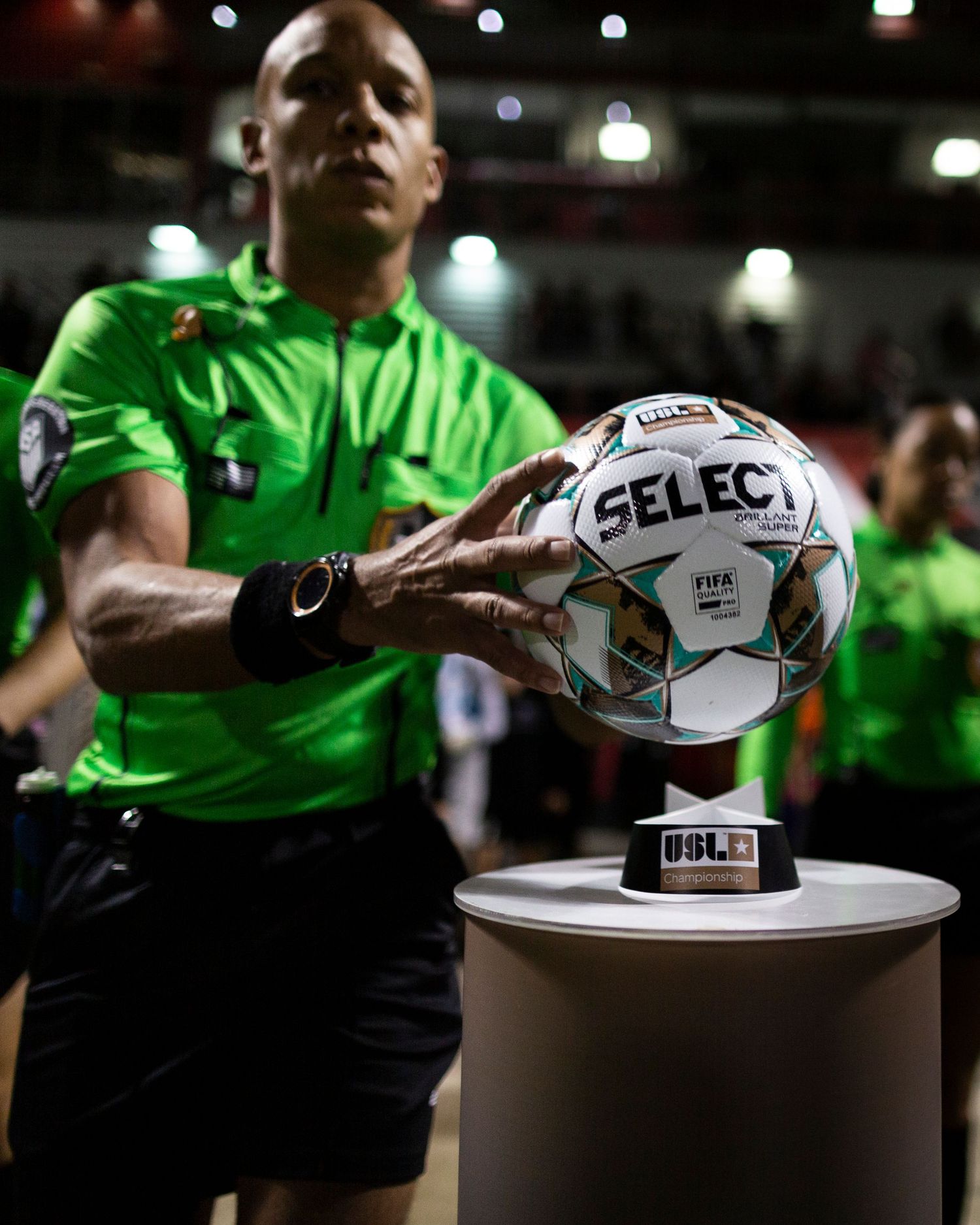 Official in green uniform places match ball on pedestal before USL game.