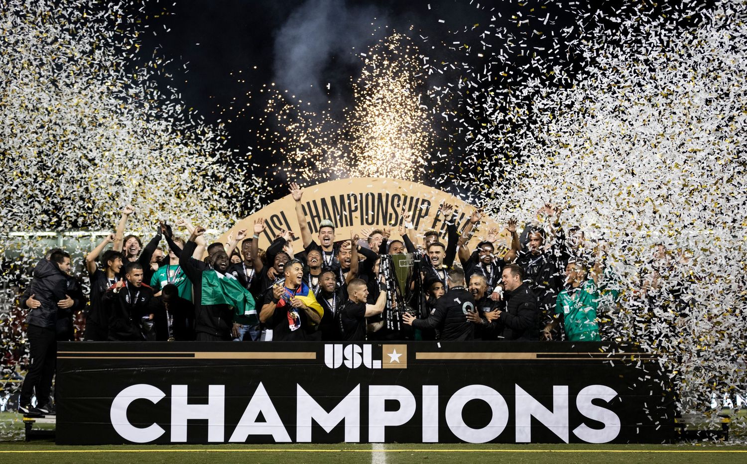 Championship celebration with confetti showering over team holding trophy on stage.