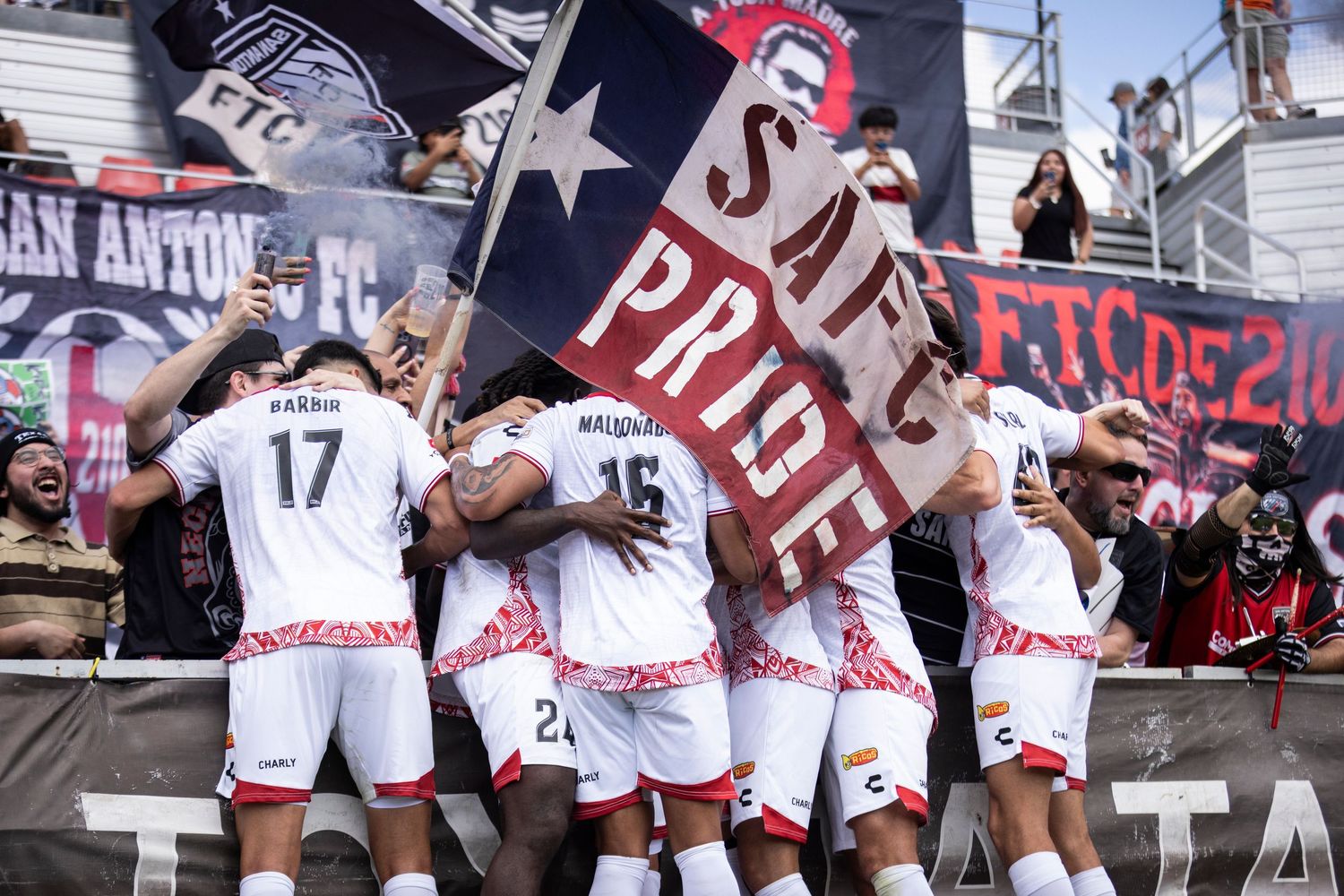 San Antonio FC players celebrate with fans holding SA Pride flag after a match.