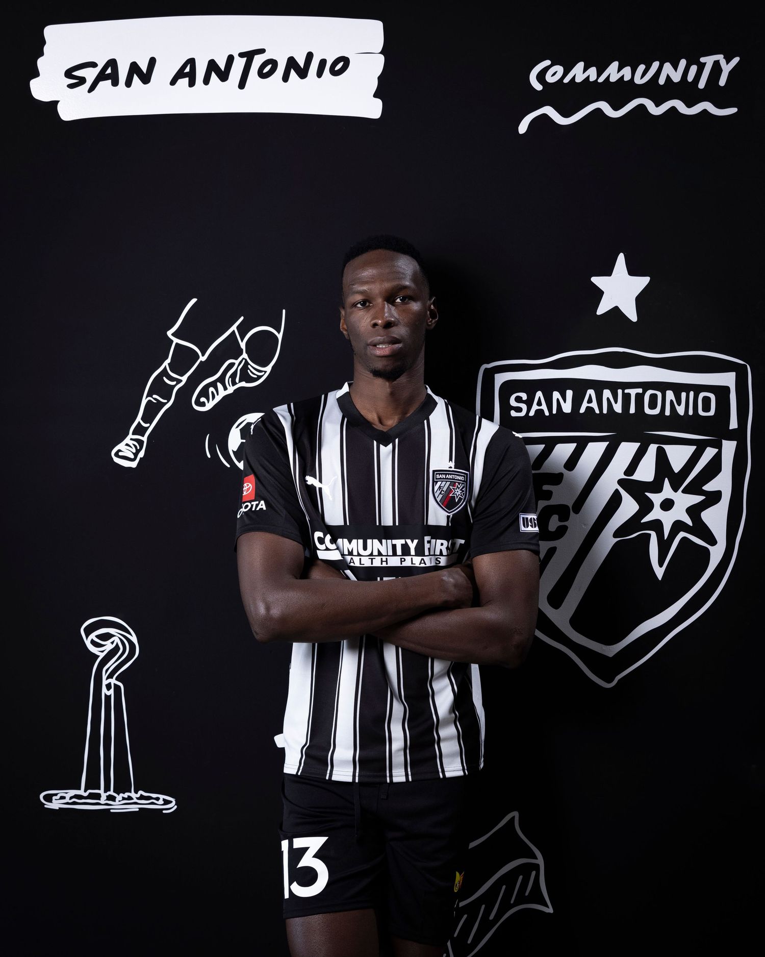 Soccer player in striped jersey poses against black wall with San Antonio themed illustrations.