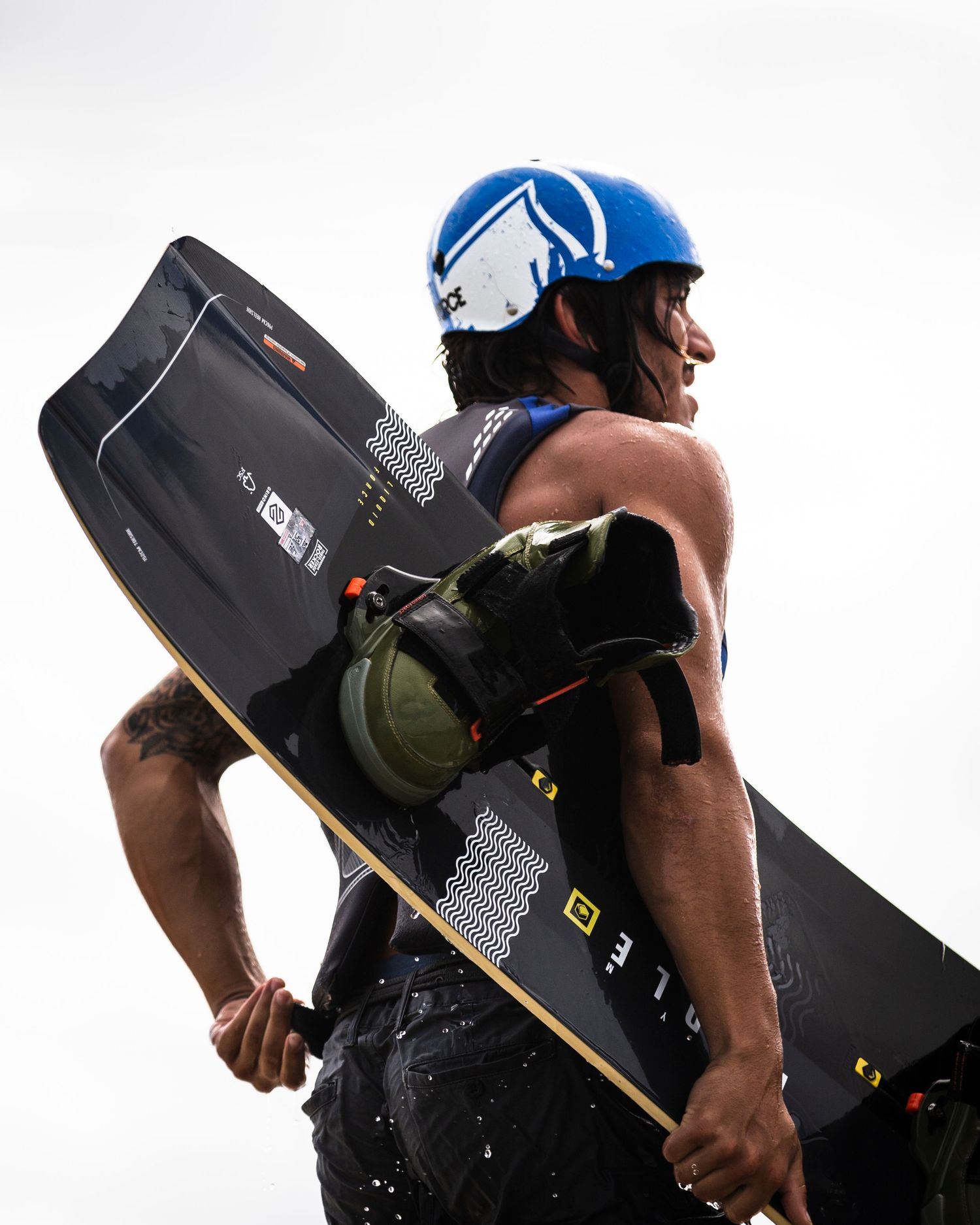 Athlete in blue helmet carrying professional wakeboard equipment against white background.