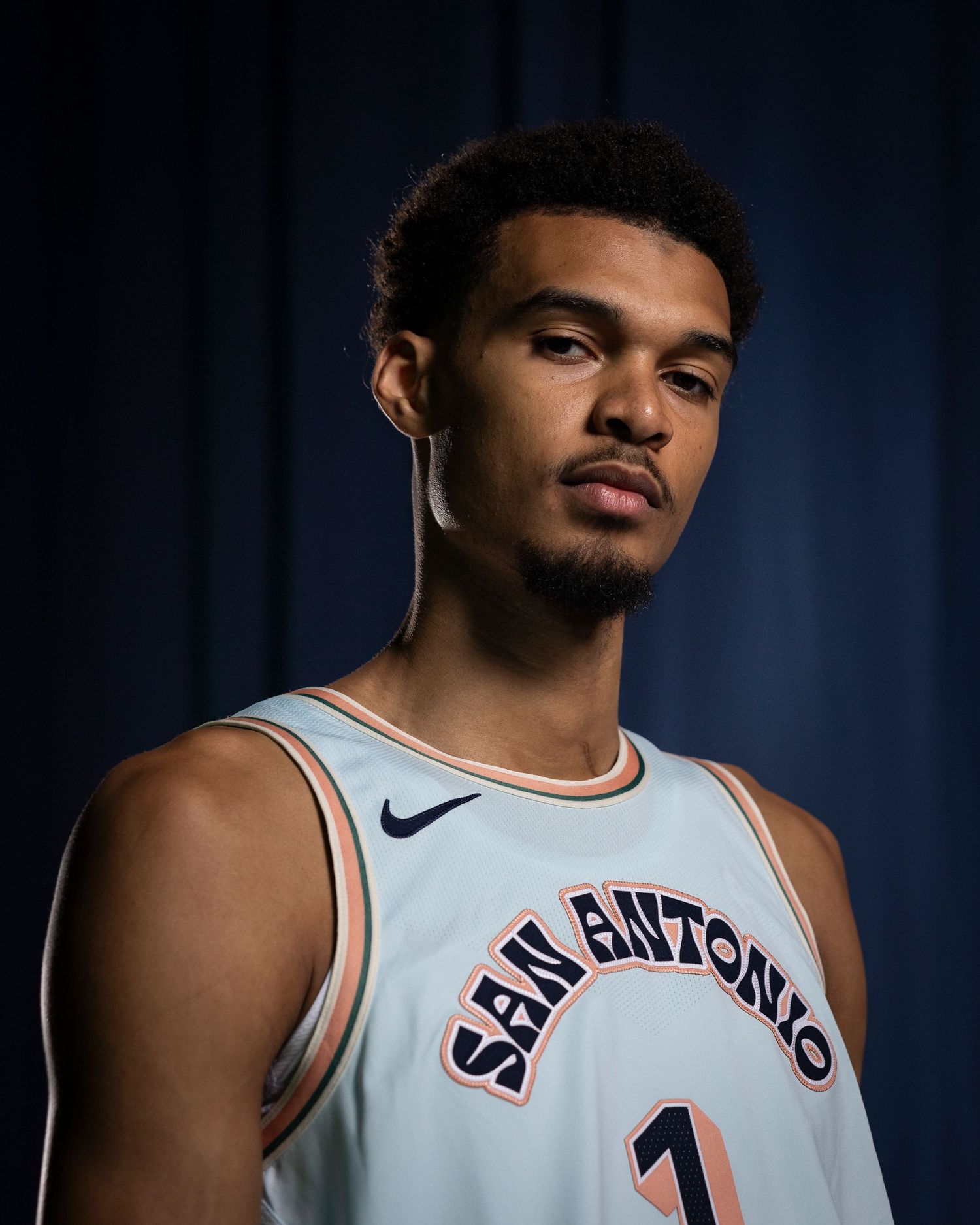 Portrait of athlete in San Antonio basketball jersey against blue backdrop.