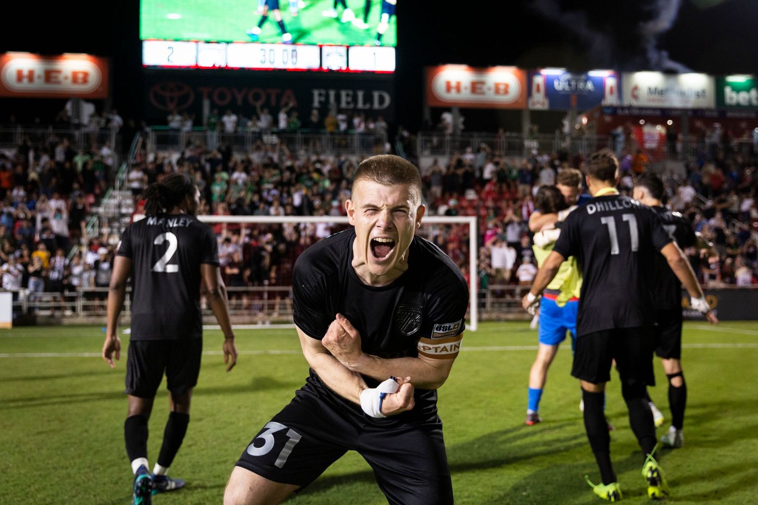 Soccer player celebrates passionately on field during nighttime match.