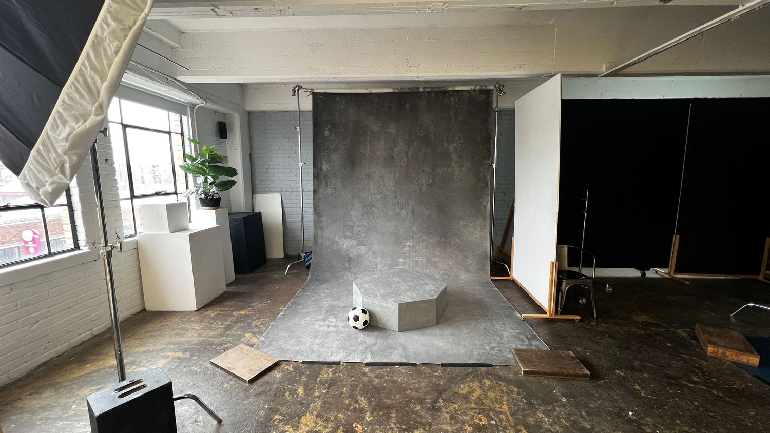A professional photography studio with a gray backdrop, lighting equipment, and scattered props on a worn concrete floor.