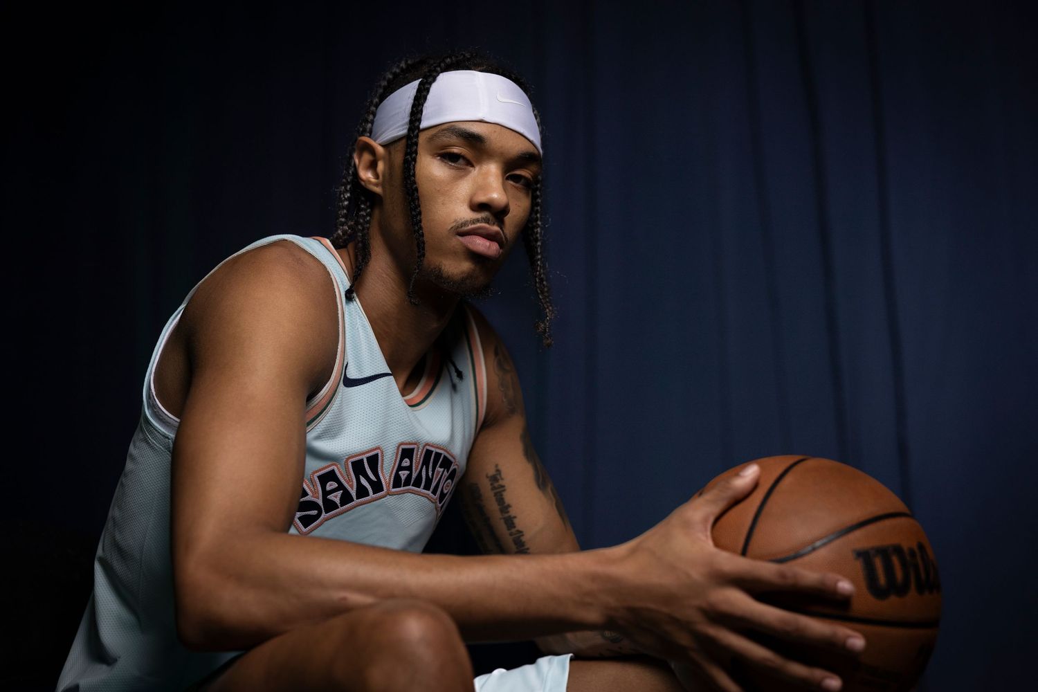 San Antonio Spurs basketball player poses with a ball in moody studio lighting.