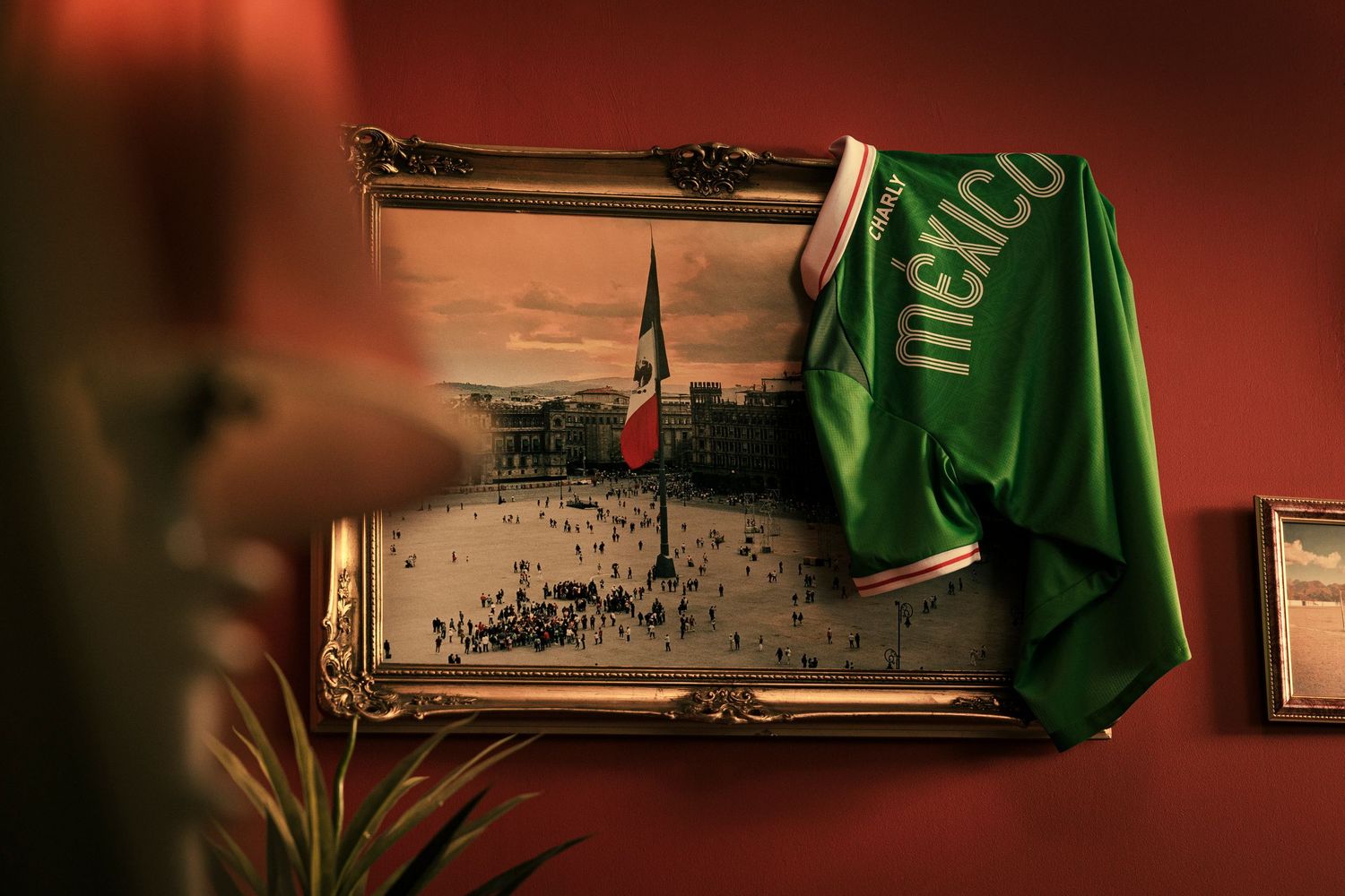 A green Mexico soccer jersey draped over a framed vintage photo on a red wall.