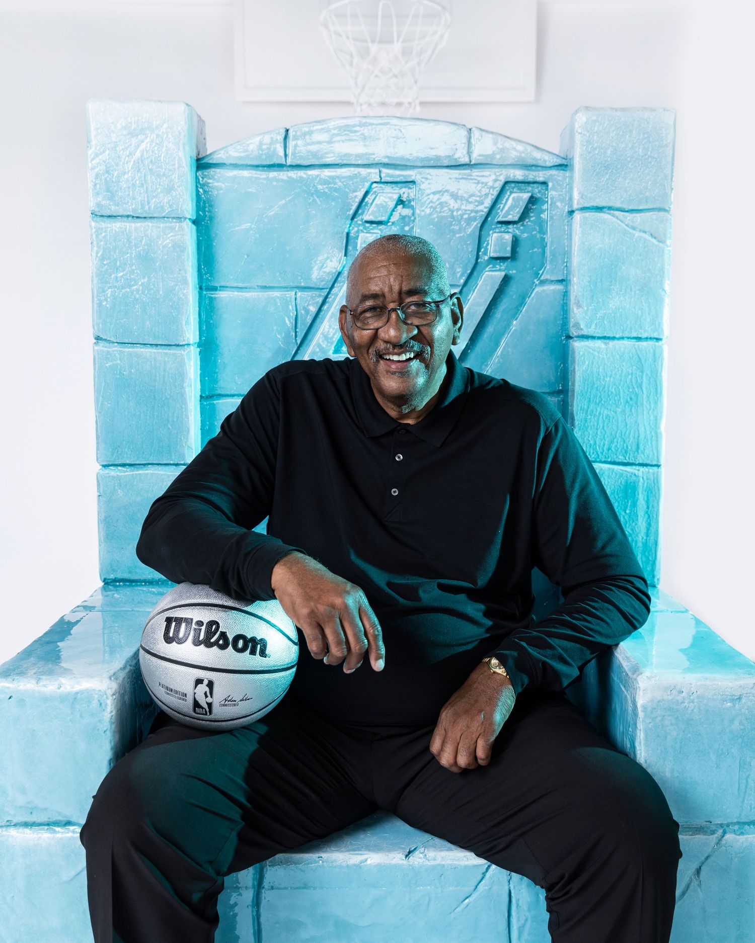 Basketball icon seated on light blue throne-like chair holding Wilson basketball.