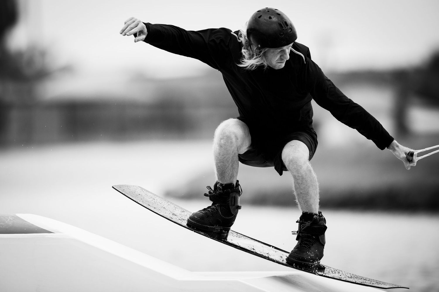 Black and white photo of wakeboarder performing grab trick over wake.
