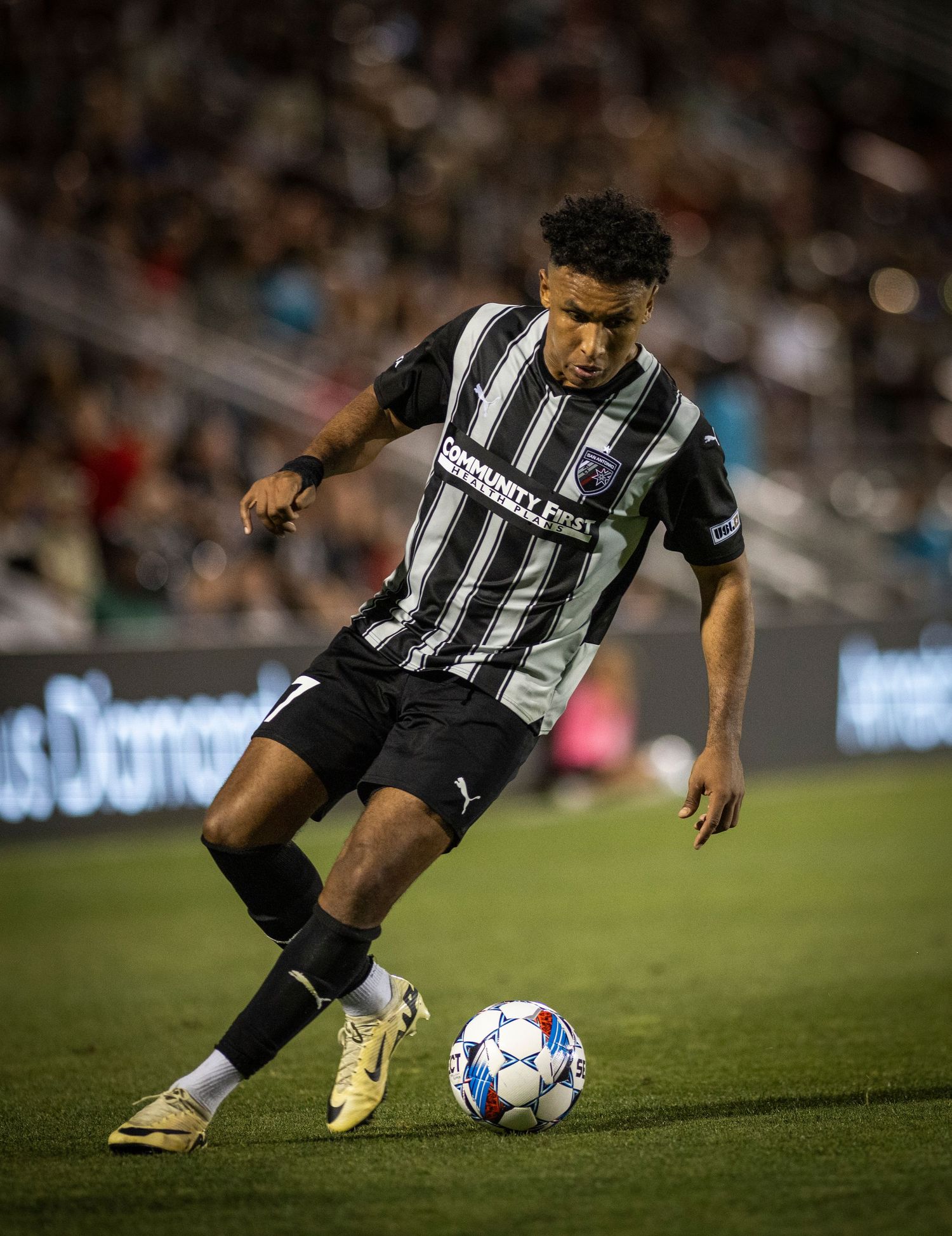 Soccer player in striped black and white uniform dribbles ball during match.