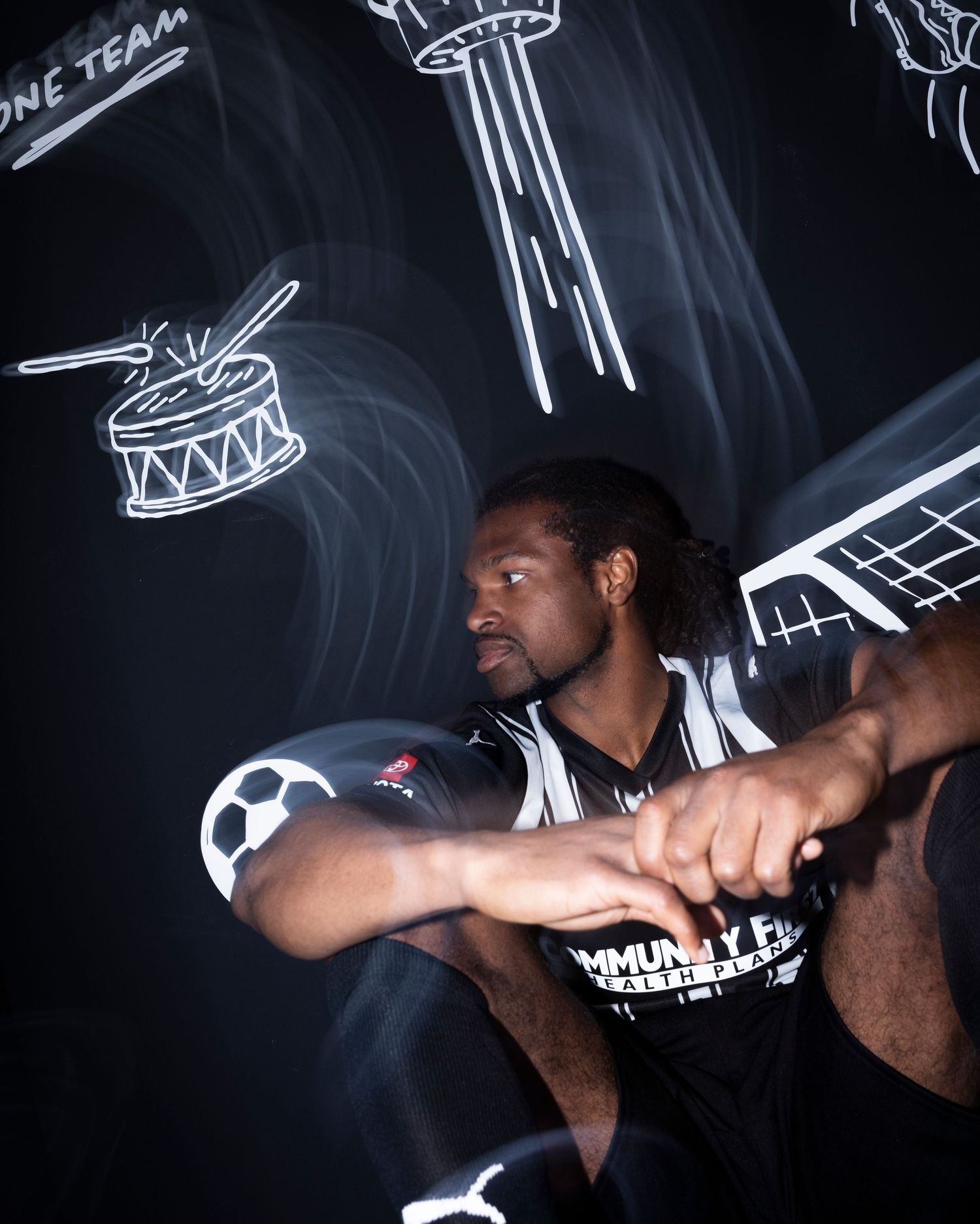 Basketball player poses against dark wall with neon sports illustrations.