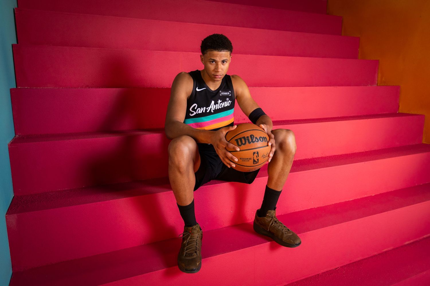 San Antonio Spurs player sits on colorful pink steps holding a basketball during a professional NBA photo shoot.