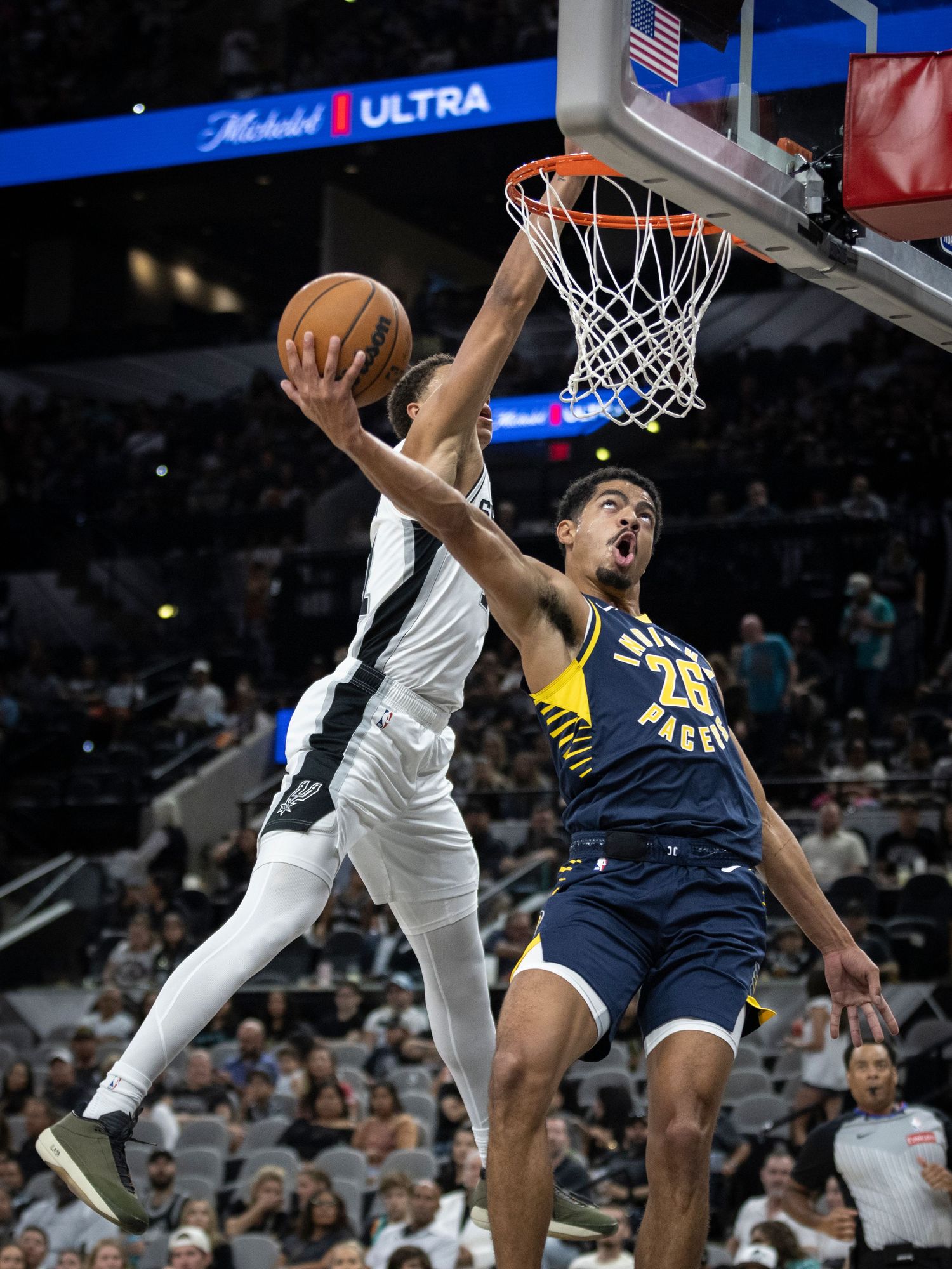 Players leap high to contest a shot at the basket during an NBA game.