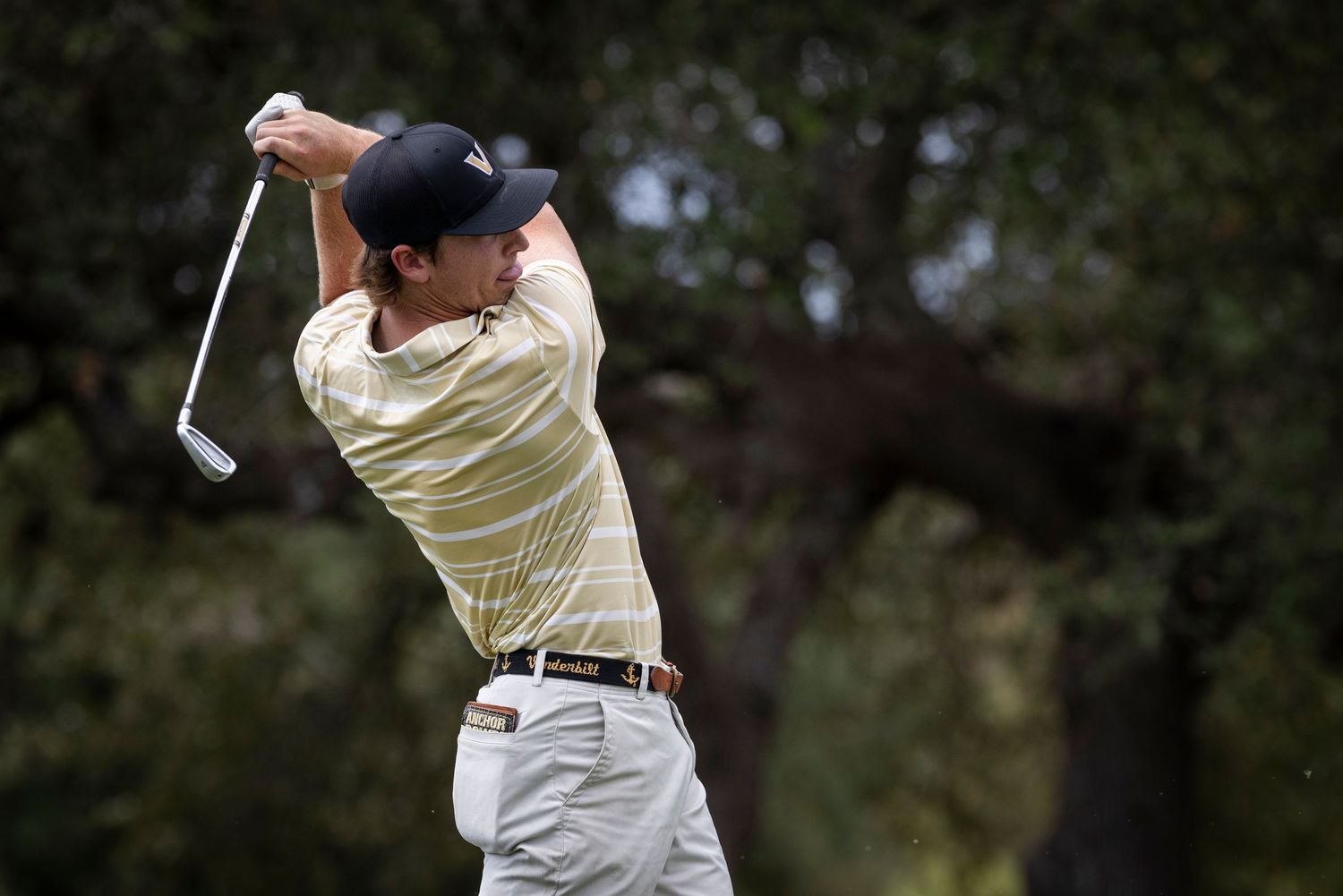 Golfer in yellow shirt and navy cap demonstrating perfect backswing form during a golf swing.