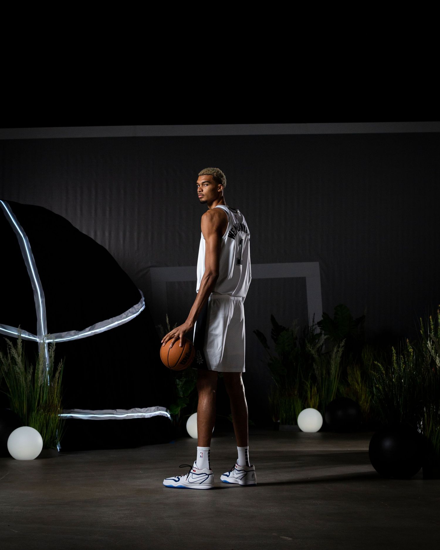 Side view of Spurs player in white uniform holding basketball in studio with dramatic lighting.