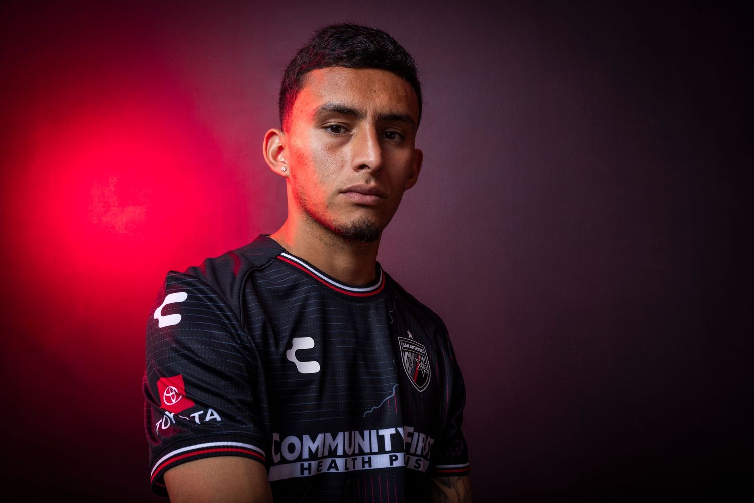 Soccer player in black jersey photographed against dramatic red lighting.