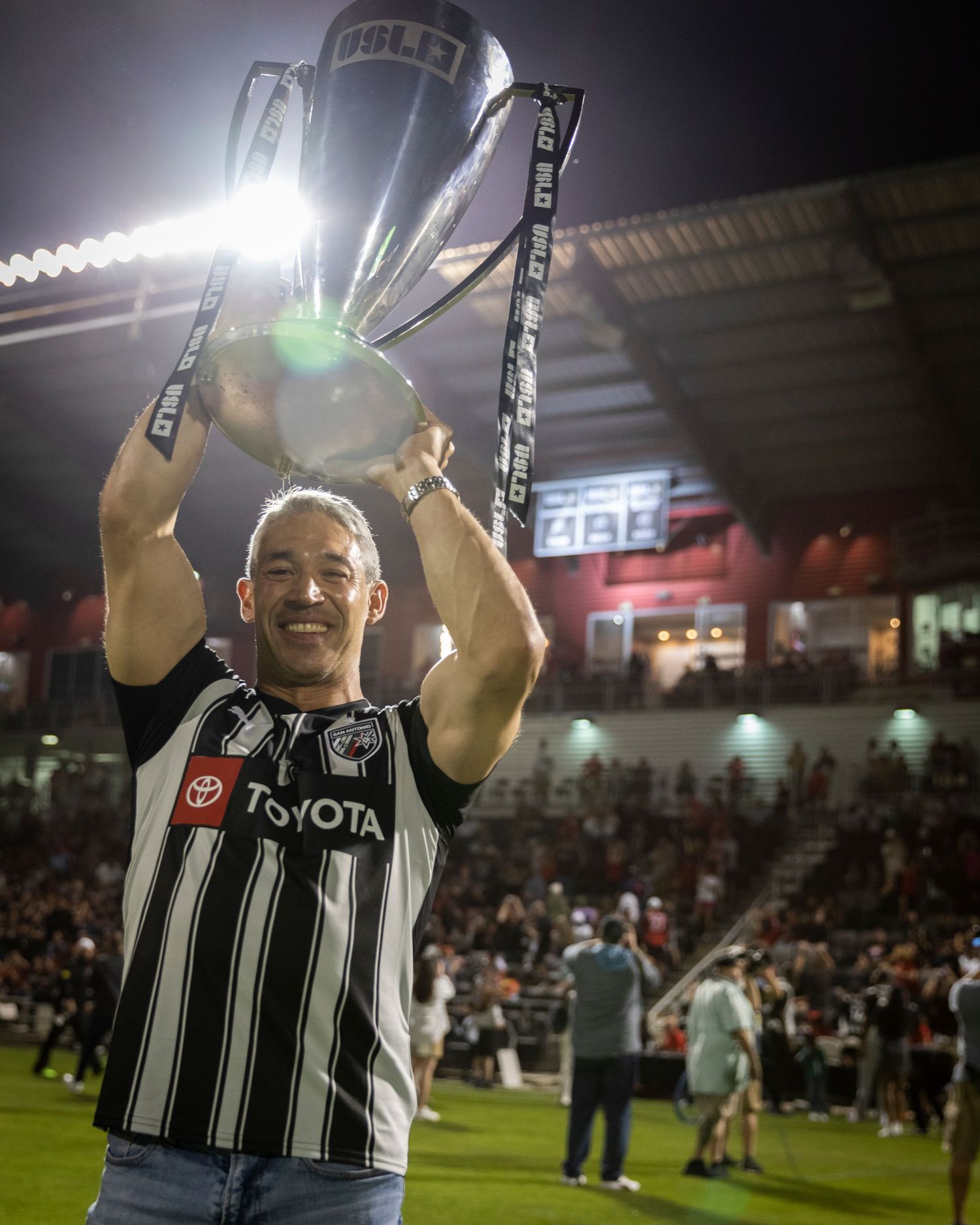 Celebration moment as trophy is lifted under stadium lights in black and white jersey.